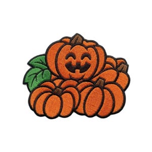 Peut inclure: Un écusson brodé représentant un groupe de trois citrouilles orange avec des tiges brunes et une feuille verte. La citrouille centrale présente un visage de lanterne d'Halloween noir brodé avec un sourire, souligné par des contours noirs.