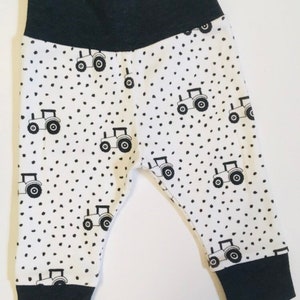 May include: White baby leggings with a black tractor and polka dot pattern. The leggings have black elastic at the waist and ankles.