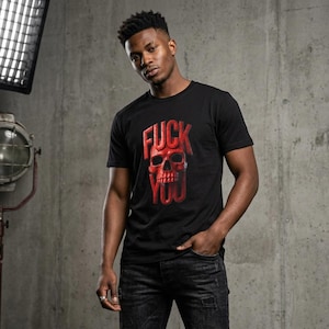 Puede incluir: Una camiseta negra de manga corta con un estampado gráfico en el pecho. El diseño consiste en un cráneo humano rojo colocado en el centro, con la palabra FUCK en letras rojas sobre el cráneo y la palabra YOU en letras rojas debajo de este.