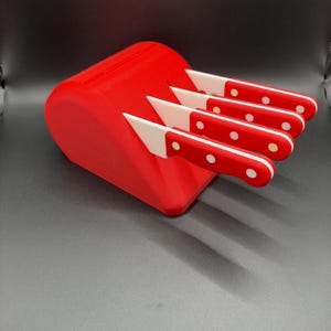 May include: A bright red knife block holding four matching knives. Each knife features a white blade and a red handle with two white circular rivets. The block is wedge-shaped with four slots, and the knives are arranged in a parallel row.