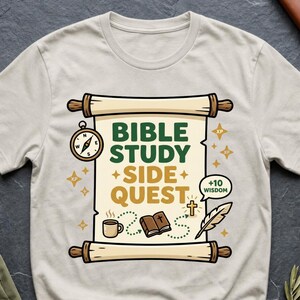 Puede incluir: Una camiseta de color beige claro con un gráfico de un pergamino con el texto BIBLE STUDY SIDE QUEST. El diseño incluye una brújula, una taza de café, un libro abierto con una cruz, una pluma y un globo de texto que dice +10 WISDOM, rodeado de estrellas XP.