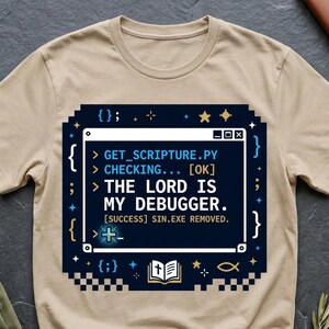 May include: A beige crew neck t-shirt featuring a dark blue graphic of a computer terminal window. The text reads: GET_SCRIPTURE.PY, CHECKING... [OK], THE LORD IS MY DEBUGGER. [SUCCESS] SIN.EXE REMOVED. The design includes code brackets and a small bible icon.