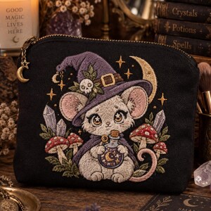 Op de afbeelding: Een zwarte etui met rits voorzien van een geborduurde illustratie van een muis met een paarse heksenhoed met schedel, die een flesje vasthoudt. Het ontwerp bevat rode paddenstoelen, kristallen, sterren en een halve maan, met een gouden maanrits.