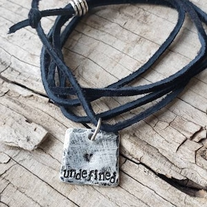 May include: A black leather cord necklace with a silver pendant that says "undefined" with a small heart above the word.