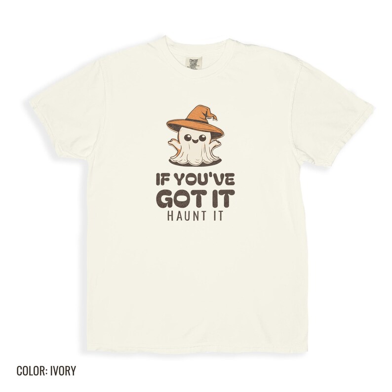 Ivory Comfort Colors t-shirt printed with the words If You'Ve Got It Haunt It and a drawing of a cute retro cartoon ghost wearing a witch hat, folded flat lay