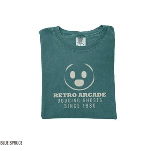 Blue Spruce Comfort Colors t-shirt printed with the words Retro Arcade Dodging Ghosts Since 1980 and a drawing of a maze with a Pac-Man character, folded flat lay