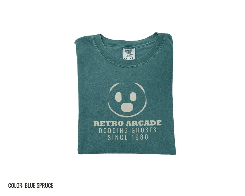 Blue Spruce Comfort Colors t-shirt printed with the words Retro Arcade Dodging Ghosts Since 1980 and a drawing of a maze with a Pac-Man character, folded flat lay