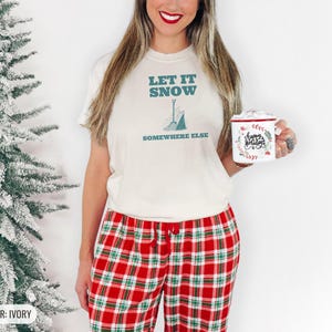 Ivory Comfort Colors t-shirt printed with the words Let It Snow Somewhere Else and a drawing of a metal snow shovel propped beside an empty bag of rock salt, worn by a woman