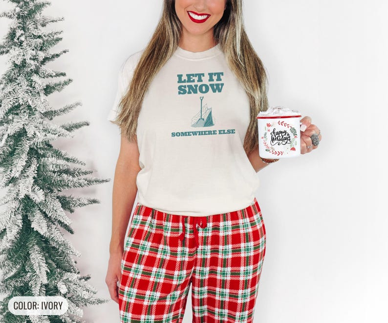 Ivory Comfort Colors t-shirt printed with the words Let It Snow Somewhere Else and a drawing of a metal snow shovel propped beside an empty bag of rock salt, worn by a woman