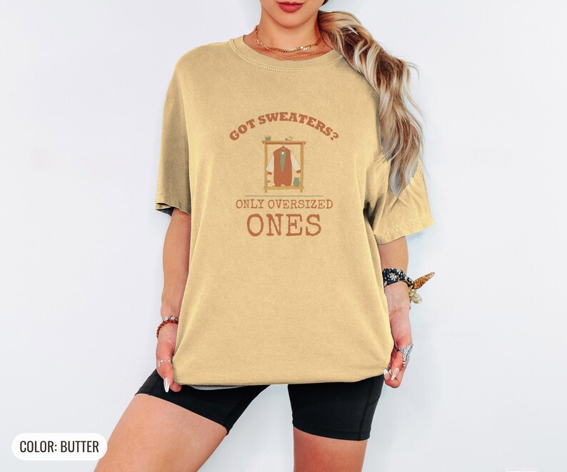 Butter Comfort Colors t-shirt printed with the words Got Sweaters? Only Oversized Ones and a drawing of a knitted wool cardigan hanging from a simple wooden clothes hanger, worn by a woman