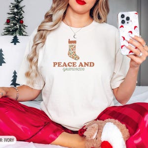 Ivory Comfort Colors t-shirt printed with the words Peace And Grandkids and a drawing of a classic knitted wool christmas stocking stuffed with small toys, worn by a woman