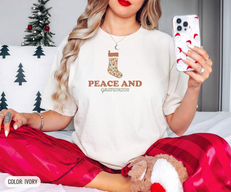 Ivory Comfort Colors t-shirt printed with the words Peace And Grandkids and a drawing of a classic knitted wool christmas stocking stuffed with small toys, worn by a woman