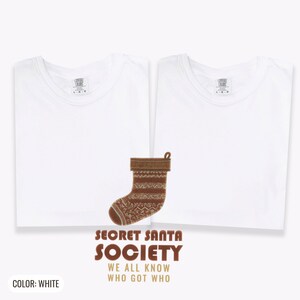 White Comfort Colors t-shirt printed with the words Secret Santa Society We All Know Who Got Who and a drawing of a knitted wool stocking stuffed with stick candy, two matching shirts
