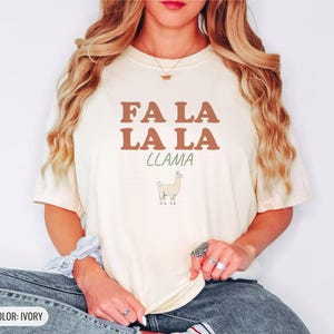 Ivory Comfort Colors t-shirt printed with the words Fa La La La Llama and a drawing of a fluffy llama, worn by a woman