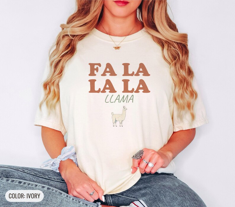 Ivory Comfort Colors t-shirt printed with the words Fa La La La Llama and a drawing of a fluffy llama, worn by a woman