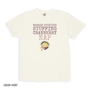 Ivory Comfort Colors t-shirt printed with the words Mashed Potatoes Stuffing Cranberry Nap and a drawing of a heavy enamel-coated cast iron Dutch oven filled with creamy mashed potatoes, steam lines, folded flat lay