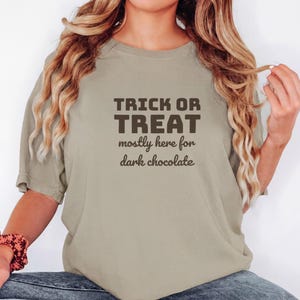 Khaki Comfort Colors t-shirt printed with the words Trick Or Treat Mostly Here For Dark Chocolate, worn by a woman