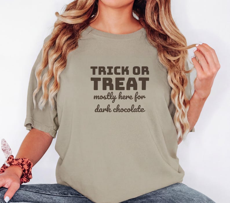 Khaki Comfort Colors t-shirt printed with the words Trick Or Treat Mostly Here For Dark Chocolate, worn by a woman