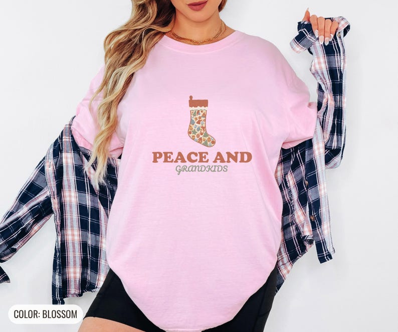 Blossom Comfort Colors t-shirt printed with the words Peace And Grandkids and a drawing of a classic knitted wool christmas stocking stuffed with small toys, worn by a woman