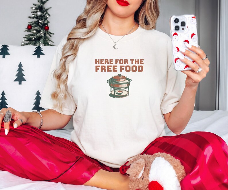 Ivory Comfort Colors t-shirt printed with the words Here For The Free Food and a drawing of a stainless steel chafing dish with steam rising off the lid, worn by a woman