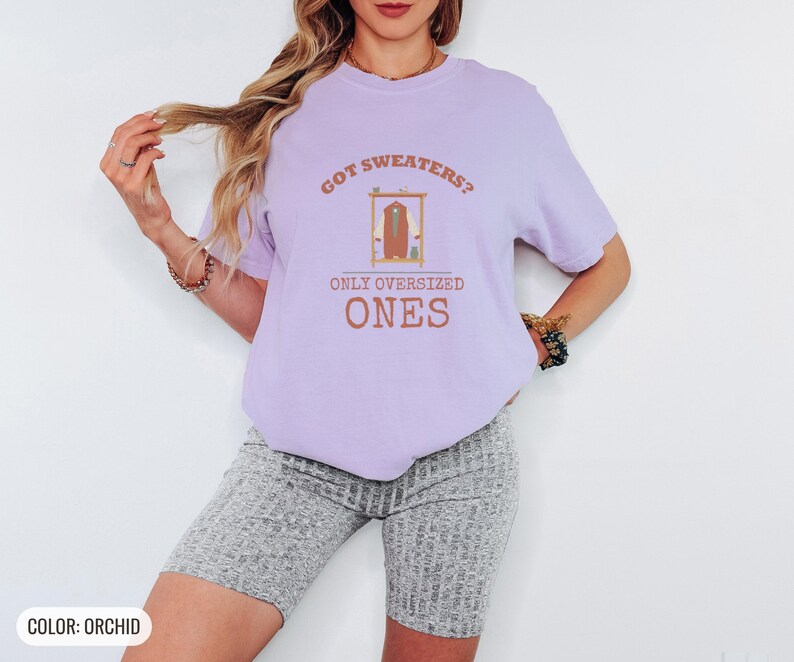 Orchid Comfort Colors t-shirt printed with the words Got Sweaters? Only Oversized Ones and a drawing of a knitted wool cardigan hanging from a simple wooden clothes hanger, worn by a woman