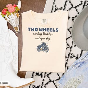 Ivory Comfort Colors t-shirt printed with the words Two Wheels Winding Blacktop And Open Sky and a drawing of a classic cruiser motorcycle in side profile, folded flat lay