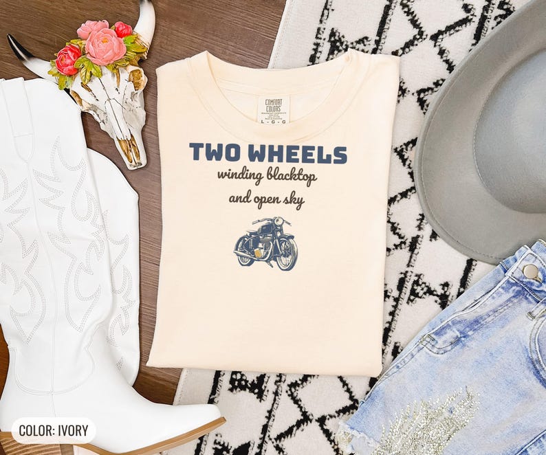 Ivory Comfort Colors t-shirt printed with the words Two Wheels Winding Blacktop And Open Sky and a drawing of a classic cruiser motorcycle in side profile, folded flat lay