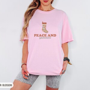 Blossom Comfort Colors t-shirt printed with the words Peace And Grandkids and a drawing of a classic knitted wool christmas stocking stuffed with small toys, worn by a woman