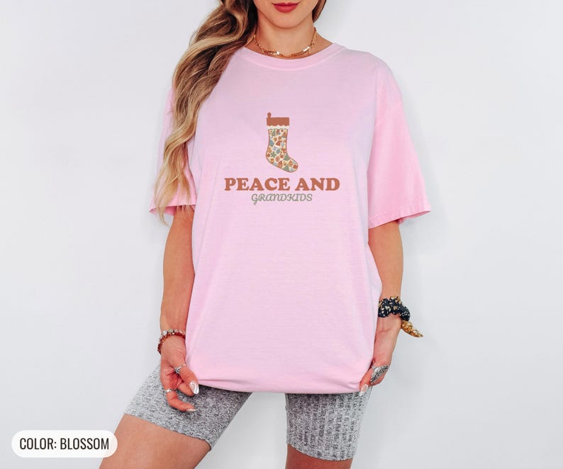 Blossom Comfort Colors t-shirt printed with the words Peace And Grandkids and a drawing of a classic knitted wool christmas stocking stuffed with small toys, worn by a woman