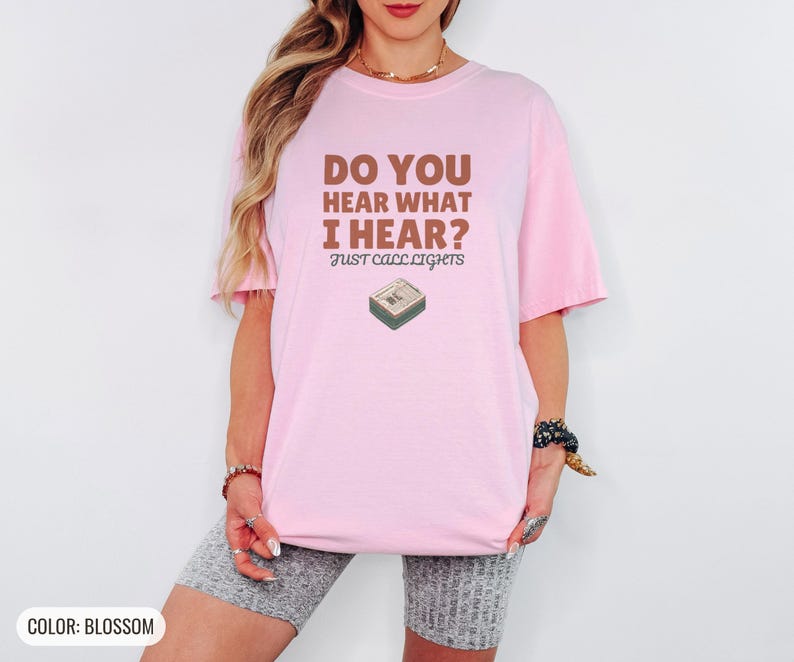 Blossom Comfort Colors t-shirt printed with the words Do You Hear What I Hear? Just Call Lights and a drawing of a rectangular electronic medical pager with a small holly sprig beside it, worn by a woman
