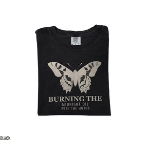 Black Comfort Colors t-shirt printed with the words Burning The Midnight Oil With The Moths and a drawing of a cecropia moth with feathery antennae, folded flat lay