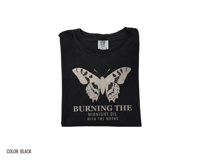 Black Comfort Colors t-shirt printed with the words Burning The Midnight Oil With The Moths and a drawing of a cecropia moth with feathery antennae, folded flat lay