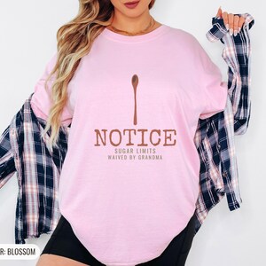 Blossom Comfort Colors t-shirt printed with the words Notice Sugar Limits Waived By Grandma and a drawing of a painted wooden spoon crossed over a cinnamon stick bundle, worn by a woman