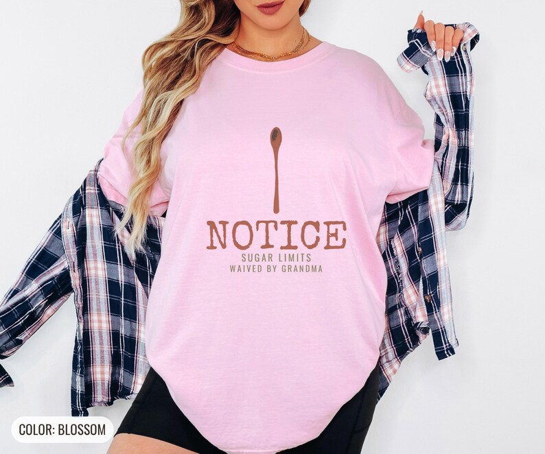 Blossom Comfort Colors t-shirt printed with the words Notice Sugar Limits Waived By Grandma and a drawing of a painted wooden spoon crossed over a cinnamon stick bundle, worn by a woman