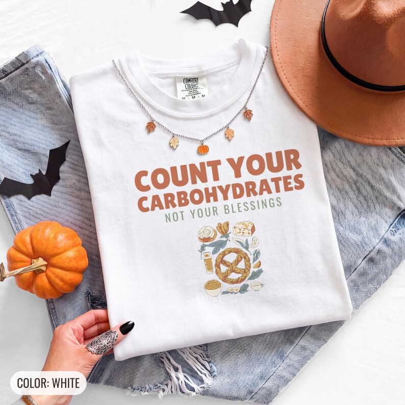 White Comfort Colors t-shirt printed with the words Count Your Carbohydrates Not Your Blessings and a drawing of a golden-brown braided pretzel with coarse salt grains, worn by a woman
