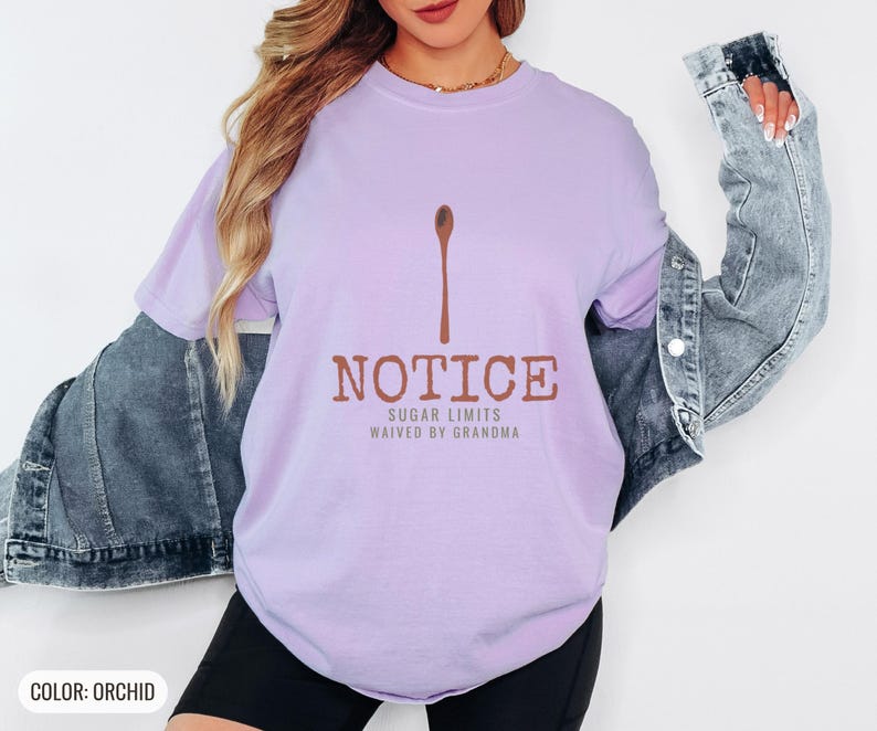 Orchid Comfort Colors t-shirt printed with the words Notice Sugar Limits Waived By Grandma and a drawing of a painted wooden spoon crossed over a cinnamon stick bundle, worn by a woman