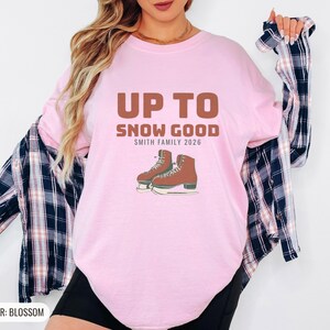 Blossom Comfort Colors t-shirt printed with the words Up To Snow Good Smith Family 2026 and a drawing of a vintage metal clamp-on ice skate with red laces, worn by a woman