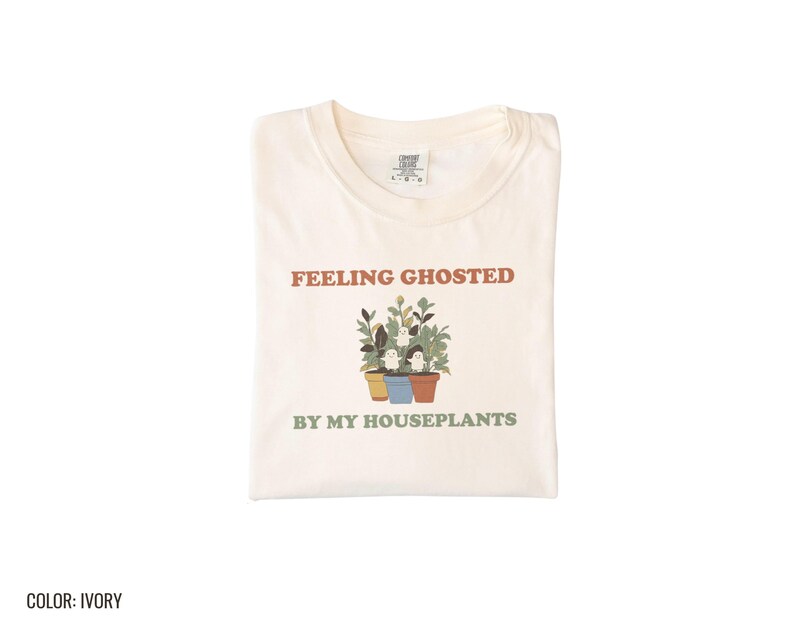 Ivory Comfort Colors t-shirt printed with the words Feeling Ghosted By My Houseplants and a drawing of a compact, self-contained group of three small potted houseplants with tiny, friendly whit, folded flat lay