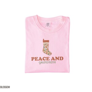 Blossom Comfort Colors t-shirt printed with the words Peace And Grandkids and a drawing of a classic knitted wool christmas stocking stuffed with small toys, folded flat lay