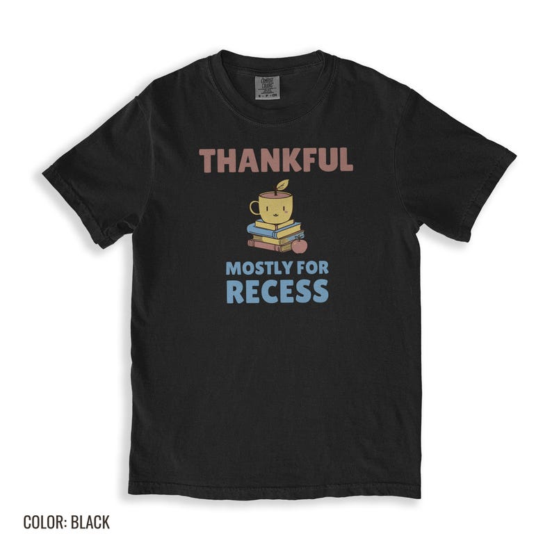 Black Comfort Colors t-shirt printed with the words Thankful Mostly For Recess and a drawing of a stack of retro school books topped with a glossy red apple and a steaming ceramic coffee, folded flat lay
