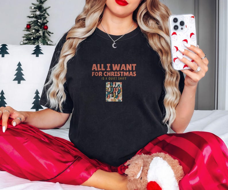 Black Comfort Colors t-shirt printed with the words All I Want For Christmas Is A Quiet Shift and a drawing of a pair of patterned compression socks hanging like Christmas stockings, worn by a woman