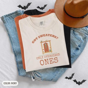 Ivory Comfort Colors t-shirt printed with the words Got Sweaters? Only Oversized Ones and a drawing of a knitted wool cardigan hanging from a simple wooden clothes hanger, worn by a woman