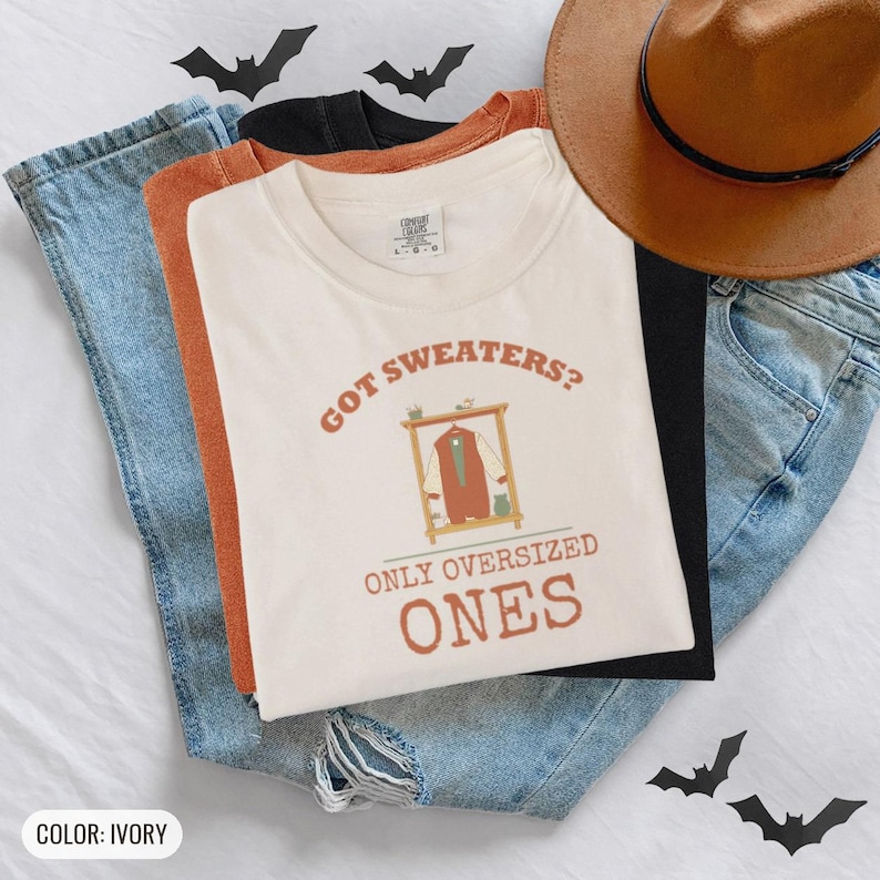 Ivory Comfort Colors t-shirt printed with the words Got Sweaters? Only Oversized Ones and a drawing of a knitted wool cardigan hanging from a simple wooden clothes hanger, worn by a woman