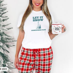 White Comfort Colors t-shirt printed with the words Let It Snow Somewhere Else and a drawing of a metal snow shovel propped beside an empty bag of rock salt, worn by a woman