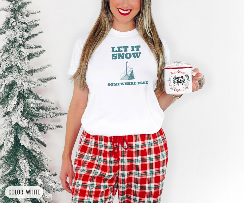 White Comfort Colors t-shirt printed with the words Let It Snow Somewhere Else and a drawing of a metal snow shovel propped beside an empty bag of rock salt, worn by a woman