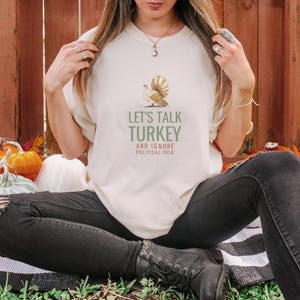 Ivory Comfort Colors t-shirt printed with the words Let'S Talk Turkey And Ignore Political Talk and a drawing of an ornate silver serving platter with turkey carving utensils, worn by a woman