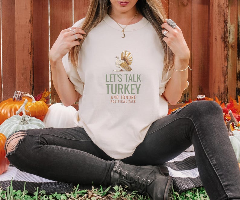Ivory Comfort Colors t-shirt printed with the words Let'S Talk Turkey And Ignore Political Talk and a drawing of an ornate silver serving platter with turkey carving utensils, worn by a woman