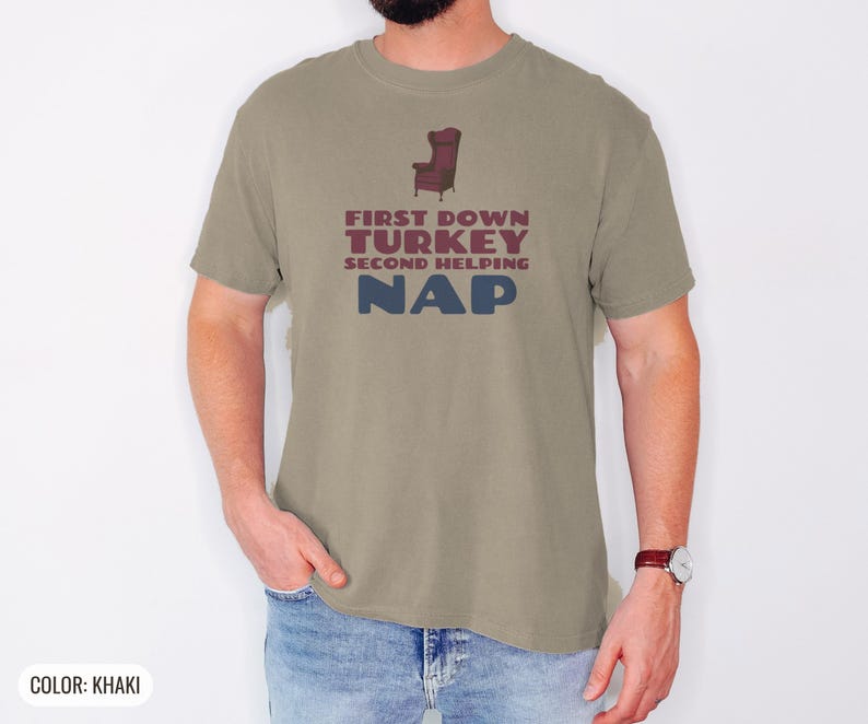Khaki Comfort Colors t-shirt printed with the words First Down Turkey Second Helping Nap and a drawing of a vintage brown recliner with a footrest extended outward, worn by a man