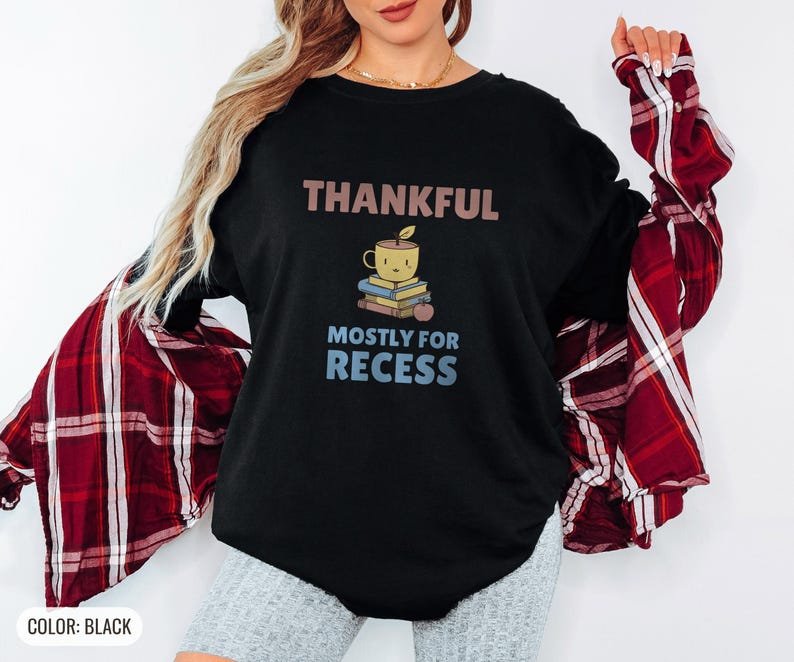 Black Comfort Colors t-shirt printed with the words Thankful Mostly For Recess and a drawing of a stack of retro school books topped with a glossy red apple and a steaming ceramic coffee, worn by a woman