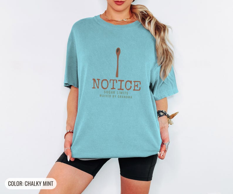 Chalky Mint Comfort Colors t-shirt printed with the words Notice Sugar Limits Waived By Grandma and a drawing of a painted wooden spoon crossed over a cinnamon stick bundle, worn by a woman